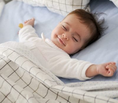 Smiling baby girl lying on a bed sleeping on blue sheets